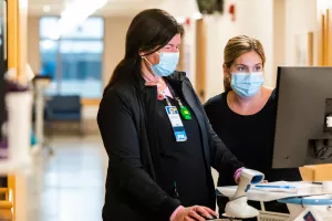 Nurses Jaclyn Rakauskas and Amanda Sullivan meeting in the hallway of Tufts Medical Center's surgical unit and reviewing information on a computer.